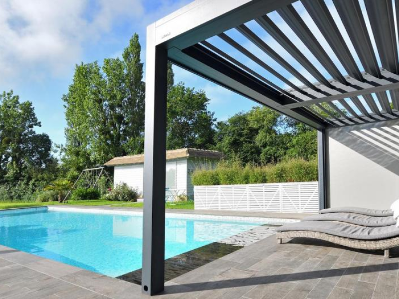 Pergola bioclimatique anthracite au bord d'une piscine avec chaises longues