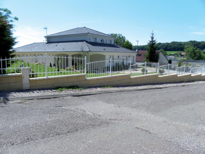 Clôture blanche à barreaux verticaux et pointes sur muret en pierre beige