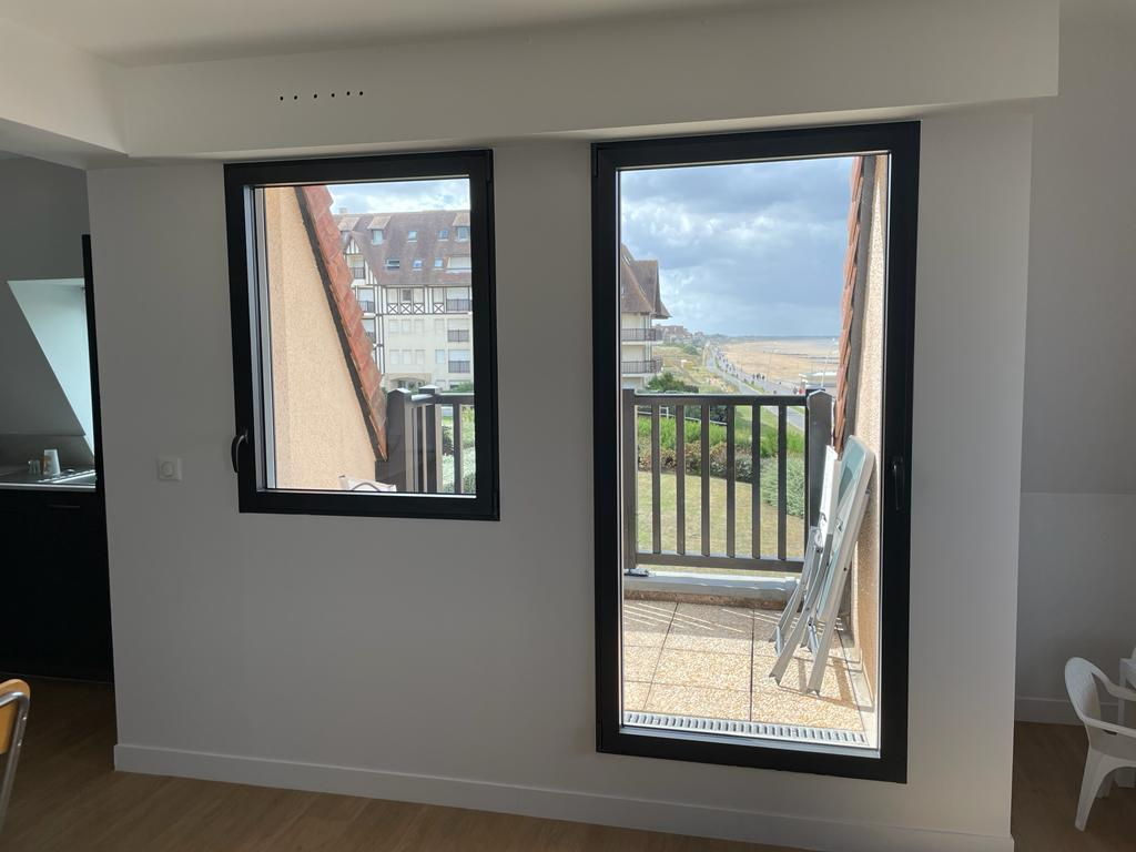 Fenêtres à cadres anthracite dans un intérieur blanc, vue sur balcon et littoral