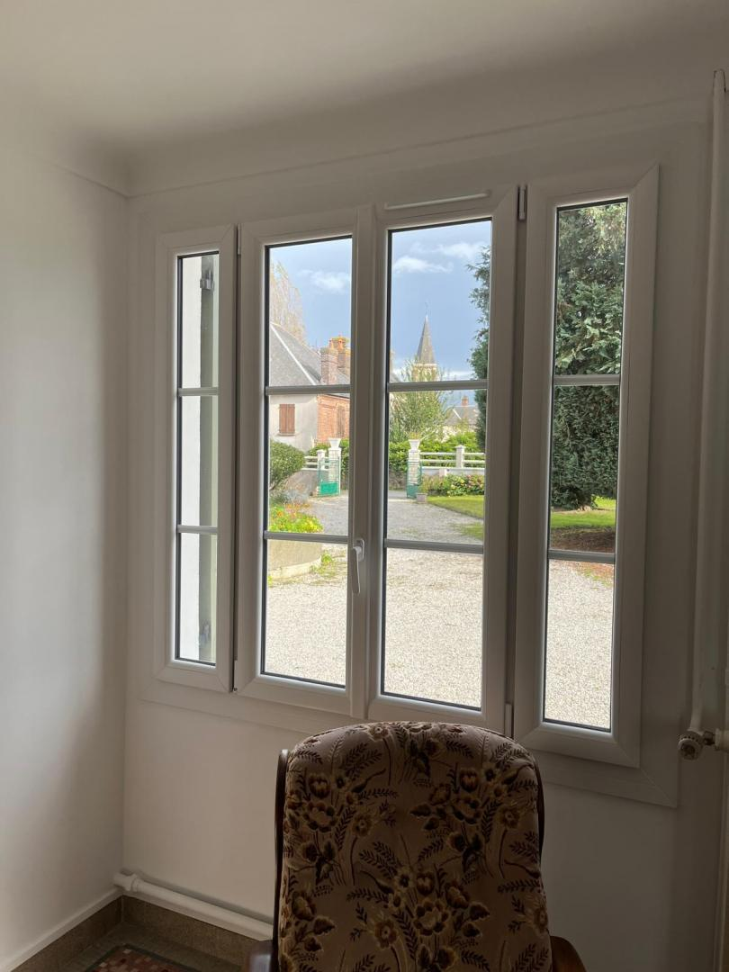 Fenêtre PVC blanche à quatre vantaux et petits bois avec vue sur clocher