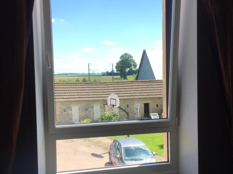 Fenêtre PVC blanche oscillo-battante avec rideaux bruns et radiateur, vue campagne