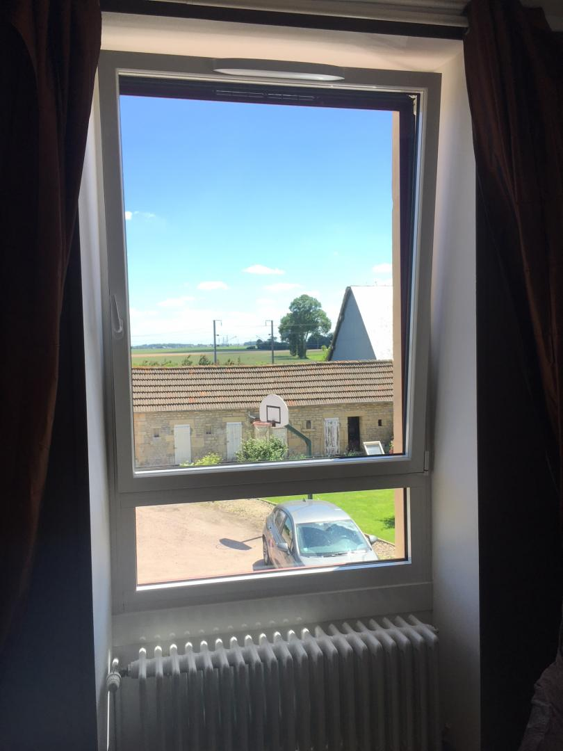 Fenêtre PVC blanche oscillo-battante avec rideaux bruns et radiateur, vue campagne