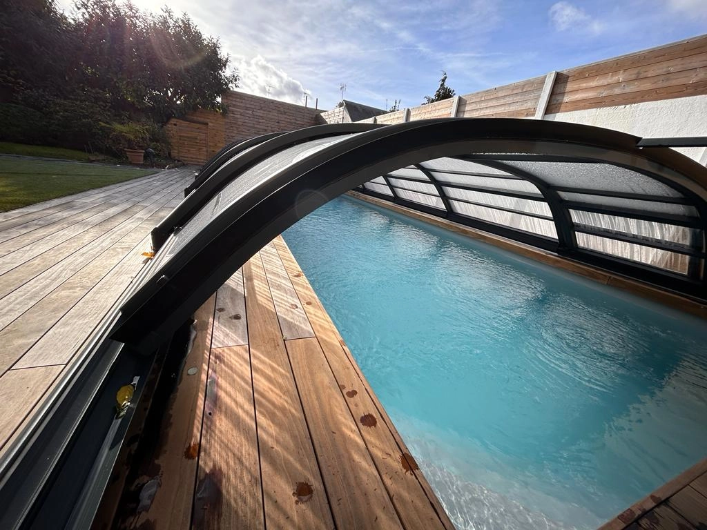 Véranda aluminium anthracite vitrée sur terrasse carrelée devant maison crème