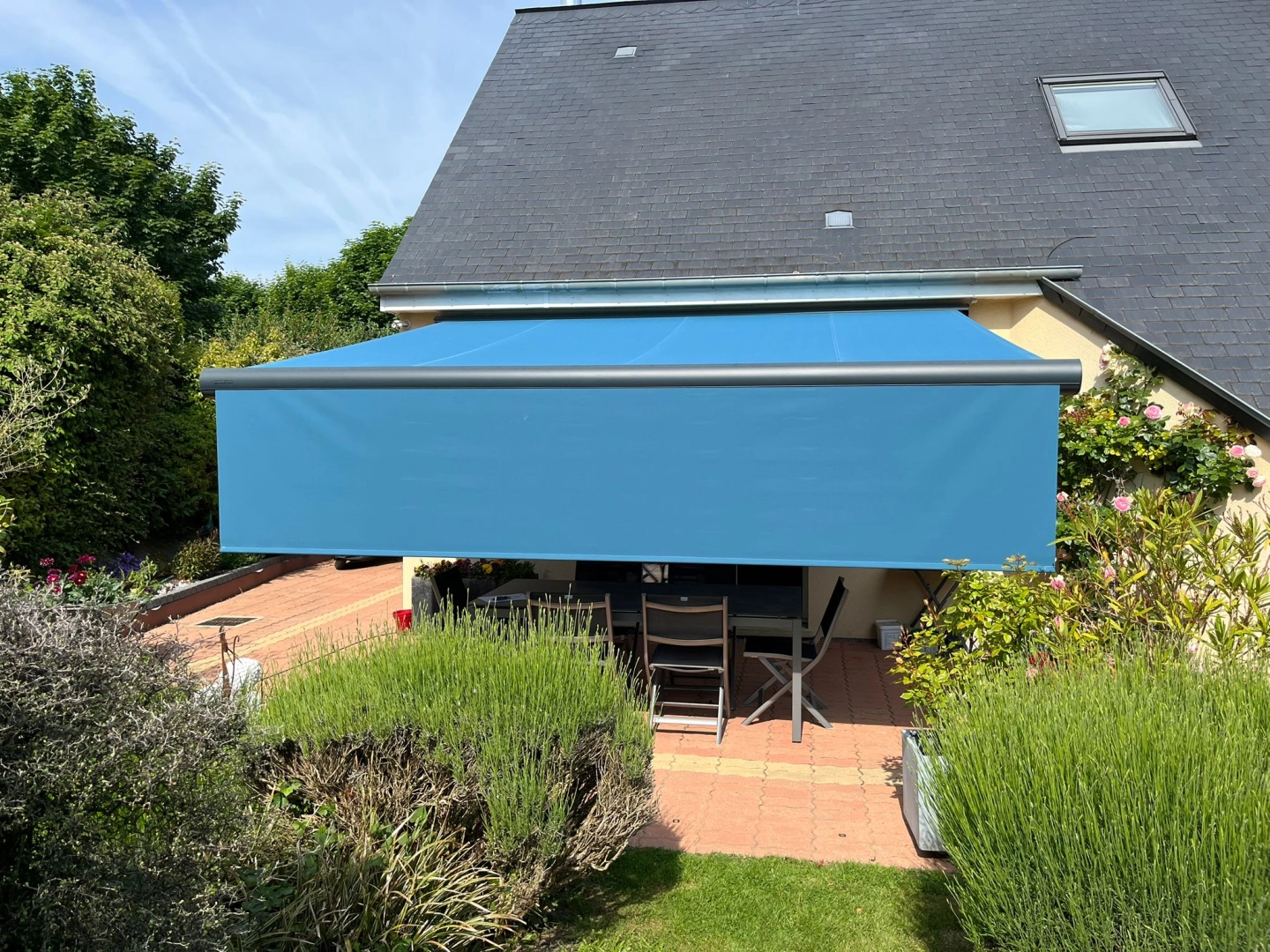Store banne turquoise déployé sur terrasse carrelée d'une maison blanche et grise