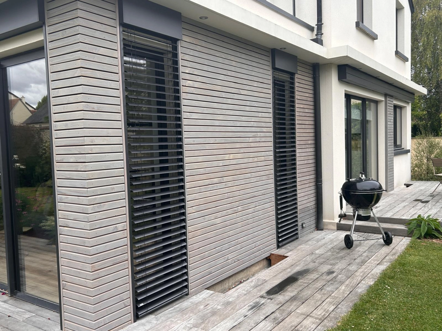 Brise-soleil orientables gris devant fenêtres noires dans une cuisine moderne