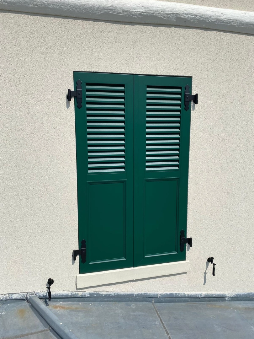 Volet pliant aluminium anthracite sur fenêtre ouverte, vue jardin et maison