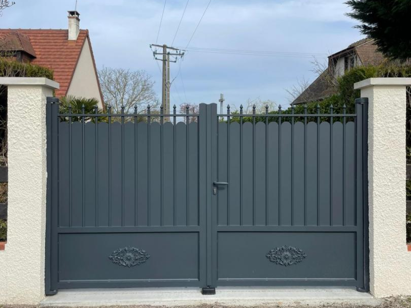 Portail battant anthracite à haut festonné et bas plein décoré, entre piliers blancs