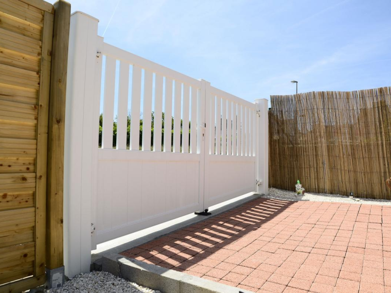 Portail battant blanc plein en bas et à barreaux en haut entre poteaux blancs