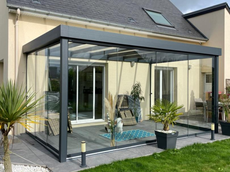 Véranda aluminium anthracite vitrée sur terrasse carrelée devant maison crème