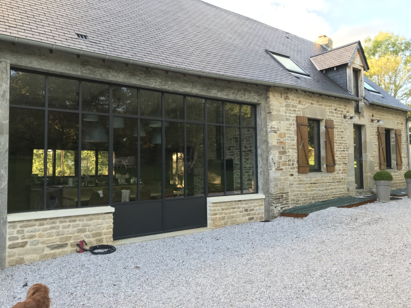 Grande verrière noire style atelier sur façade en pierre, volets bois et ardoise