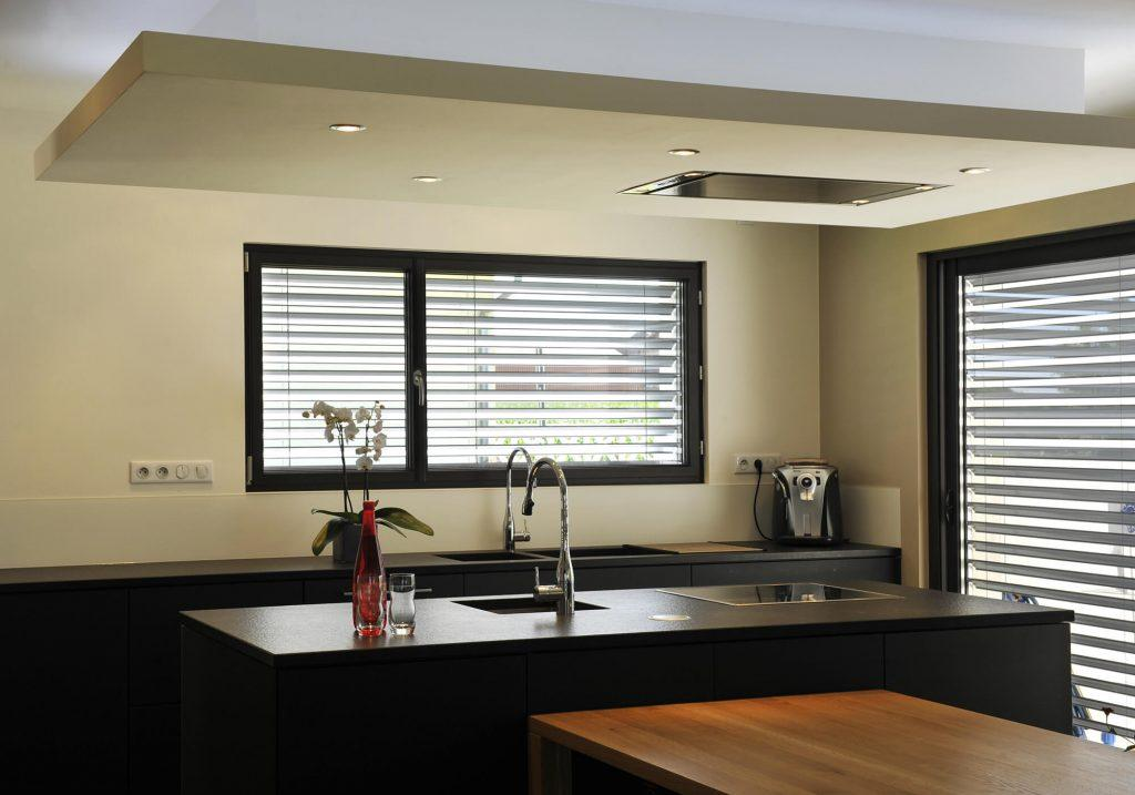 Brise-soleil orientables gris devant fenêtres noires dans une cuisine moderne