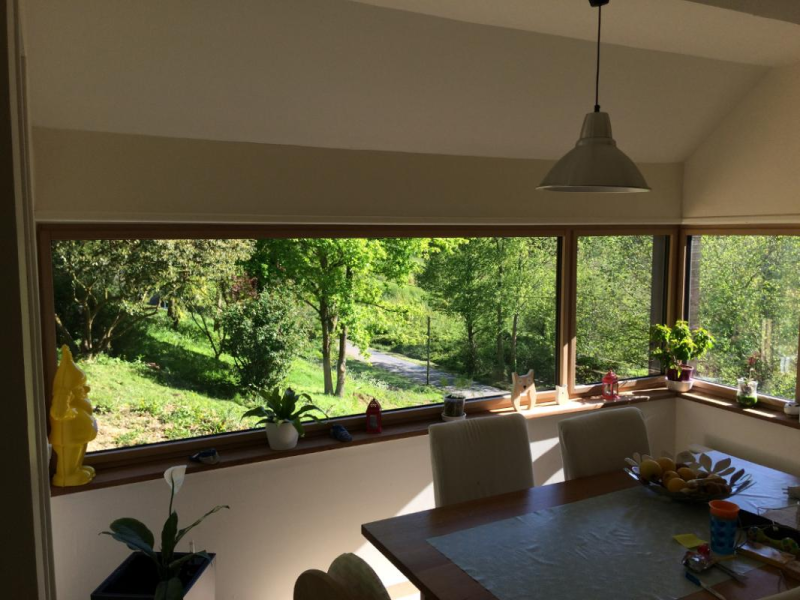 Fenêtre d'angle aspect bois clair avec vue sur jardin, table et chaises blanches