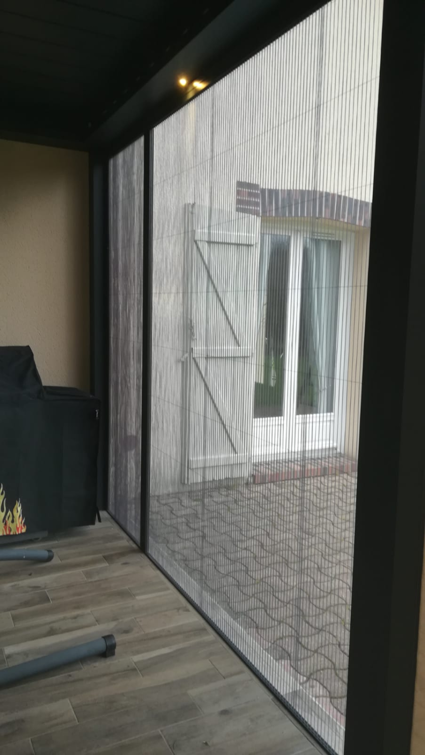 Moustiquaire plissée grise dans cadre anthracite, vue sur cour pavée