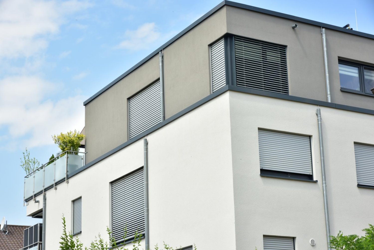 Volets roulants et brise-soleil gris sur façade blanche et grise d'immeuble