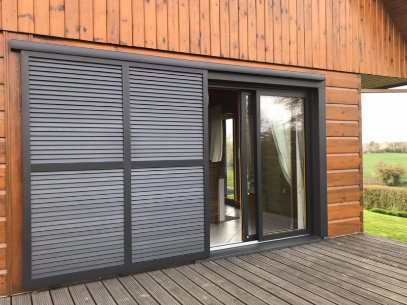Volets coulissants anthracite à lames horizontales sur chalet bois et terrasse
